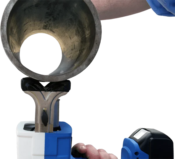 Person holding a blue and white handheld power tool positioned beneath a cylindrical metal pipe