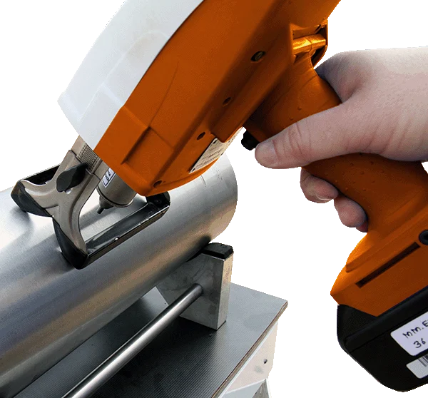 A hand holding an orange and white handheld testing tool applied to a metal pipe