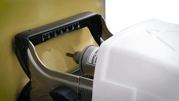 A machine tool drills into a yellow surface next to a numbered measurement scale
